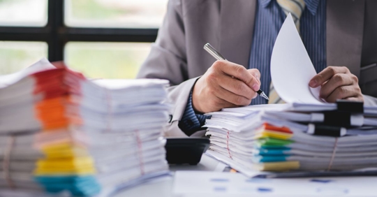 Professional reviewing stacks of paperwork on his desk.